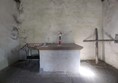 Image of alter. The alter is in the center and is a plain wooden beam. To the left there is a small row of church candles next to it. To the right is a crucifix in the corner possibly made of driftwood.