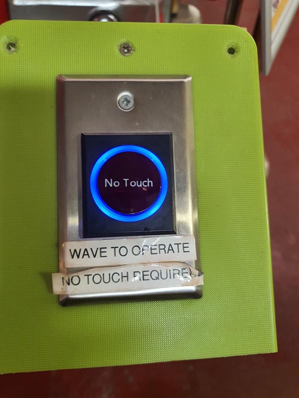 Close up image of the interactive button saying you can wave at it, that no touch is required.