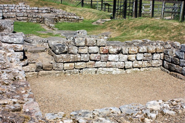 Ruins of a Roman room with fencing and steps in the background.