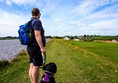 Looking back towards the main facilities, the accessible grass path stretches out into the distance. Yellow flowers line both sides of the path but it is plenty wide enough.