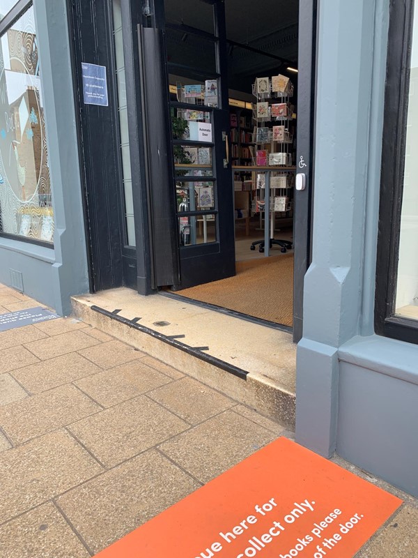 Exterior of the shop showing the step to get inside. There is a doorbell next to the door with a wheelchair symbol.