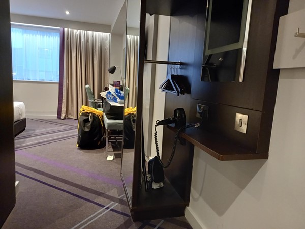 View from door into room. Mirror and hairdryer on the right. Looking into wardrobe. Table and fridge on right side, bed to the left