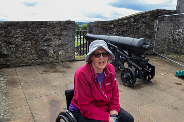 Lady in wheelchair on castle walls with cannon behind her.