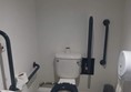 Accessible toilet, missing the emergency pull cord, who's electronics box is circled in red in the top left corner. 

The room is too narrow for wheelchairs to park next to the toilet for a transfer.