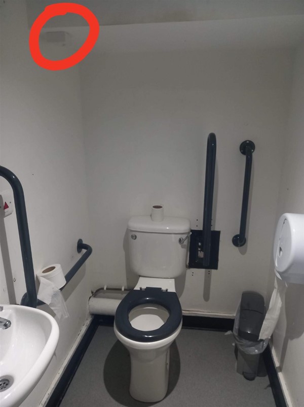 Accessible toilet, missing the emergency pull cord, who's electronics box is circled in red in the top left corner. 

The room is too narrow for wheelchairs to park next to the toilet for a transfer.