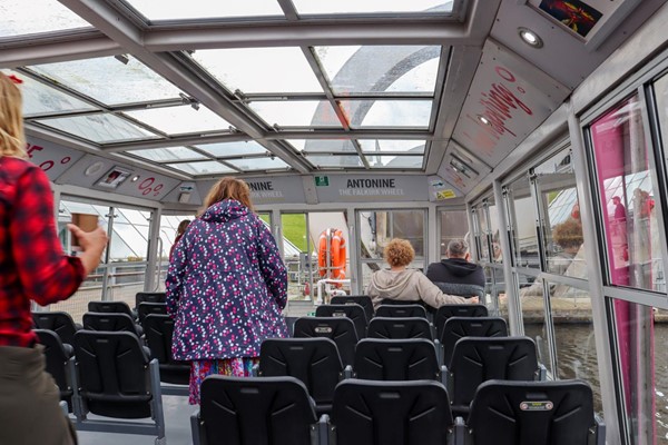 People beginning to board. There are rows of plastic seats in sets of three. The walks and ceiling are all glass.