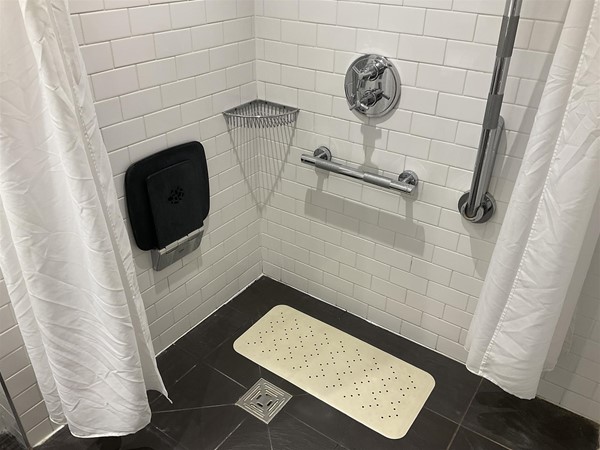 Image of a shower with white shower curtains and a white mat