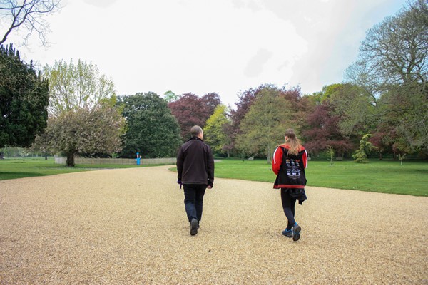 Very wide sweeping gravel path going between beautifully kept lawns with trees around and in the distance.