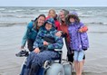 A group of people standing behind a person in a wheelchair on a beach