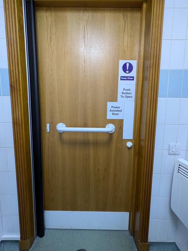 Image of the accessible toilet door,  which has dark wood and white grabrail