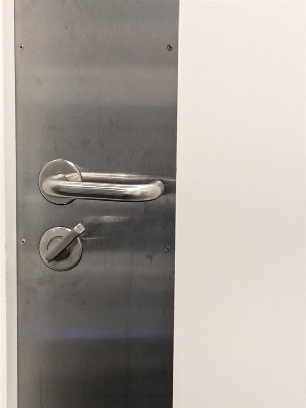 Image of the door handle inside of the toilet, a metal panel with a large handle and turning lock