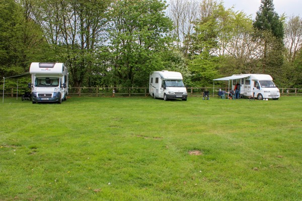 Campsite field with our three motorhomes parked at one end. The grass is uneven and slopes downwards a little.