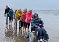 A group of people pushing a wheelchair on a beach