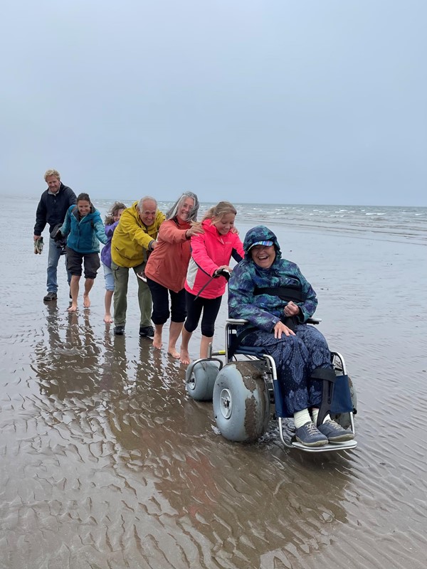 A group of people pushing a wheelchair on a beach