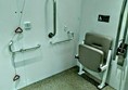 Extra large fitting room with alarm cord handles and folding seat for wheelchair users.