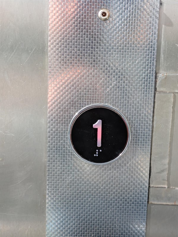 Image of the lift button. A silver 1 on a black button with braille making below