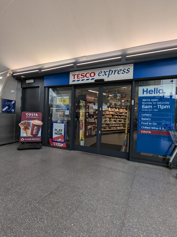 Exterior of Tesco Express at Dundee Railway Station. Blue red and white signage reads "Tesco Express". Opening times and a list of services are on the window to the right.