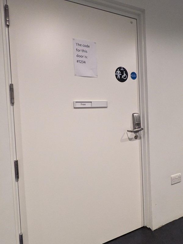 Image of the changing places door. There is a touch pad above the door handle and the code for the door is printed on a piece of paper stuck to the door.