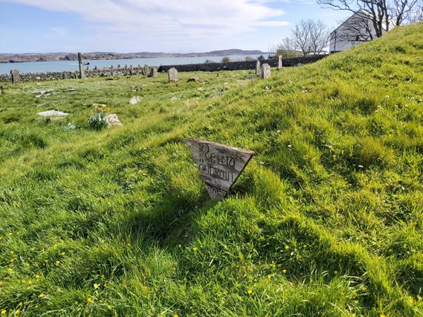 Image of the grass-covered graveyard with gravestones visible. The sea is in the background.