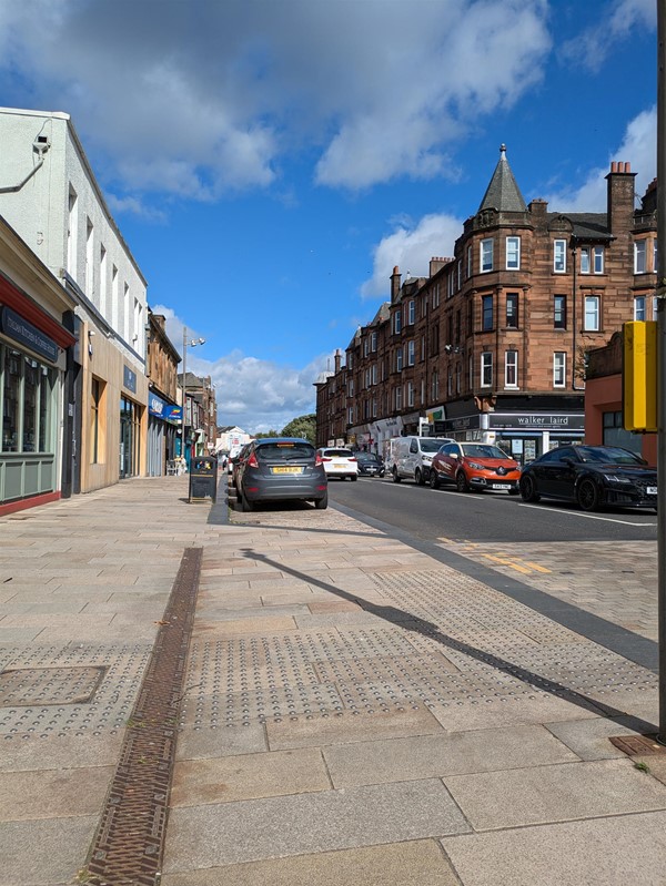 Image of the traffic lights and local on-street parking. There is tactile paving at the lights.