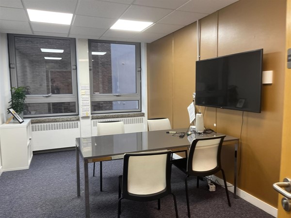 A meeting room with a 4-seater table, two big windows and a wall-hanging TV. There is a white cabinet at the corner of the room.