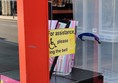 The entrance to the shop with a sign showing a wheelchair symbol and the words 'For assistance please ring the bell'. The doorbell button unit is missing.