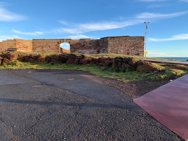 The stone wall with the archway in it and flat ground in the foreground