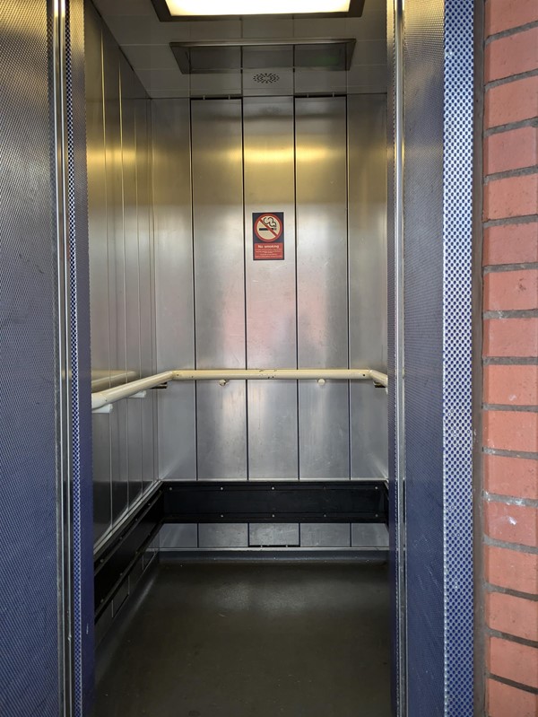 Image of lift access, the doors are open. The lift is silver on the inside with a white grab rail