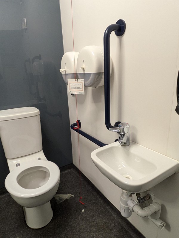 Image of the accessible toilet, a low small sink with a lever tap and grabrails on either side