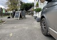 Image of a person with a dog by an A-board in a carpark with a grey car