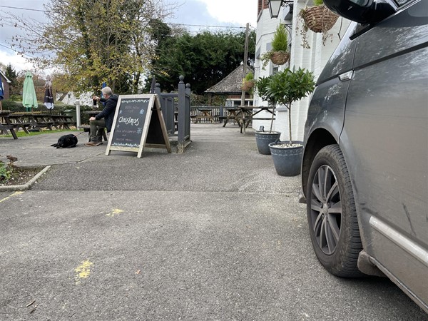 Image of a person with a dog by an A-board in a carpark with a grey car