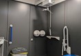 Image of the ceiling track hoist, toilet and bin. There are grab rails on the toilet which has a blue seat.