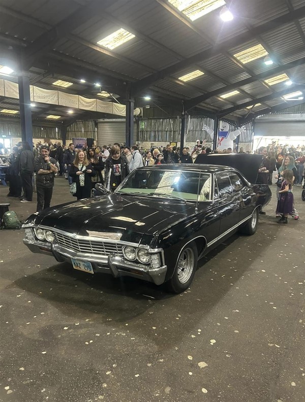 Image of a black car parked in a large room with people around it